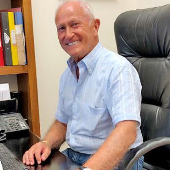 Alan d founder Alan Hemmings sitting at computer desk smiling.